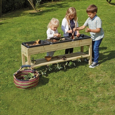 Crianças a brincar com mesa de cultivo de madeira e caixas pretas no jardim