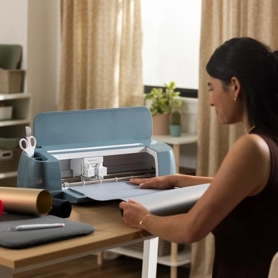 Impressora de recorte azul com mulher manuseando papel em mesa de madeira