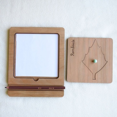 Conjunto em madeira com quadro de desenho, lápis e peça decorativa com folha desenhada.