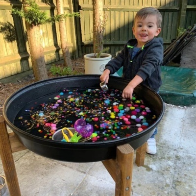 Mesa de atividades para crianças com bandeja preta redonda e bolinhas de espuma coloridas