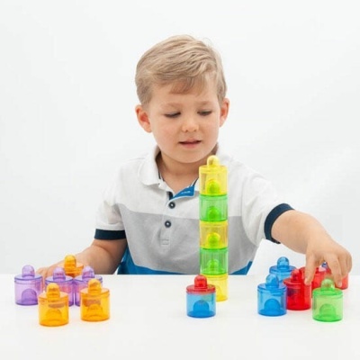 Criança a brincar com peças plásticas coloridas empilhadas numa mesa