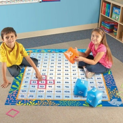Tapete educativo com números e crianças sentadas a jogar com dados grandes.