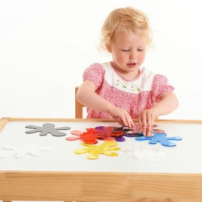 Criança vestida de rosa a brincar com peças coloridas em mesa branca de madeira.