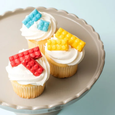 Três cupcakes com decoração de blocos coloridos em cima num prato cinzento