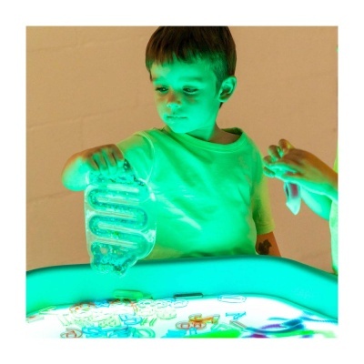 Criança com t-shirt branca a brincar com brinquedo transparente em mesa iluminada.