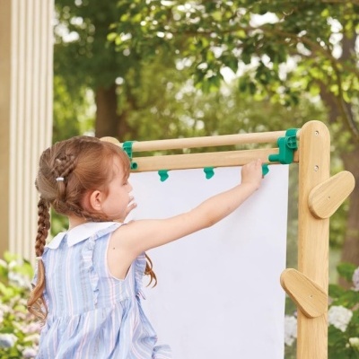 Menina a usar cavalete de madeira com papel branco ao ar livre