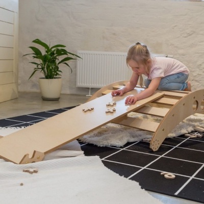 Criança a brincar numa tábua de equilíbrio de madeira num quarto com tapetes e planta