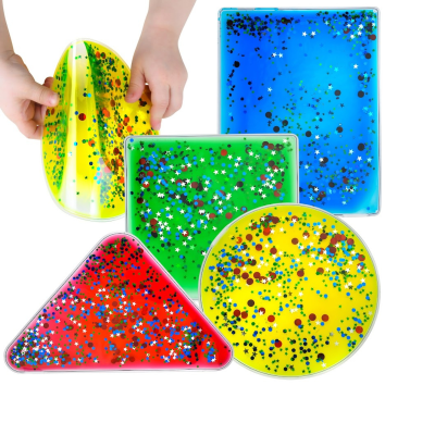 Almofadas sensoriais em formas geométricas com líquido colorido e glitter dentro, duas mãos segurando uma delas