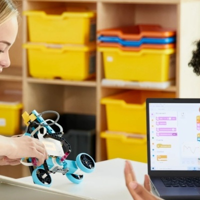 Crianças com robot educativo azul e branco e computador portátil com programação