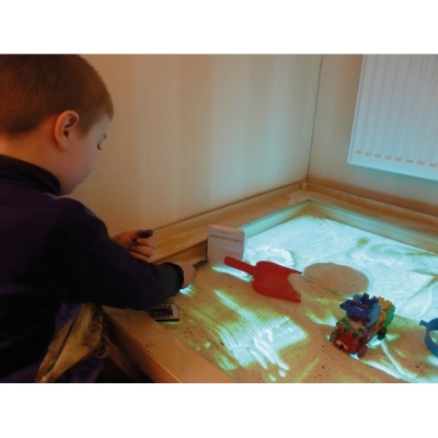 Criança a brincar numa mesa de areia luminosa com brinquedos