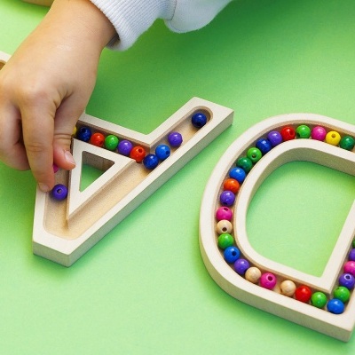 Peças de madeira de letras com contas coloridas a ser montadas por uma mão