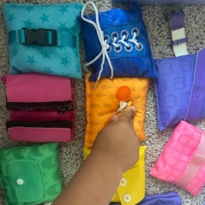 Almofadas têxteis coloridas com fechos variados e mão de criança a tocar na almofada laranja