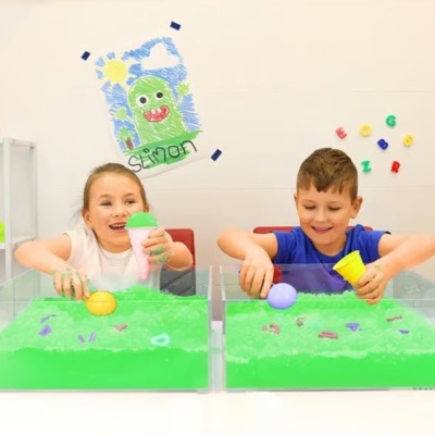 Crianças a brincar com areia cinética verde em caixas transparentes