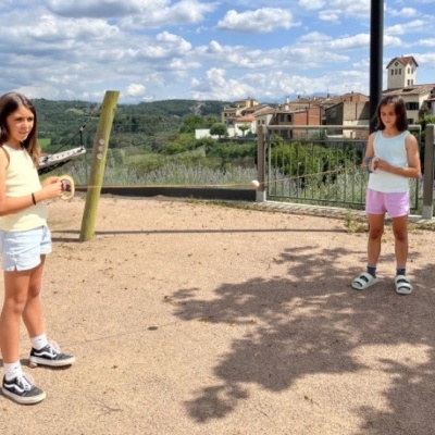 Duas meninas a usar uma corda elástica preta ao ar livre com casas ao fundo