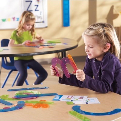 Criança a brincar com peças de plástico colorido numa mesa em sala de aula