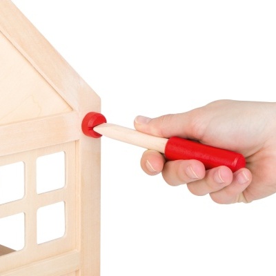 Mão segurando ferramenta de madeira com cabo vermelho numa casa de madeira clara em miniatura