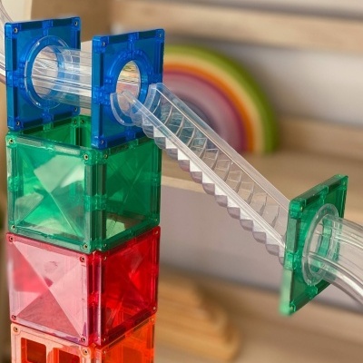 Estrutura de brinquedo modular colorida em plástico translúcido com tubos e rampa em ambiente interior.