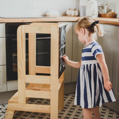 Criança a desenhar em quadro negro de torre de aprendizagem em madeira numa cozinha