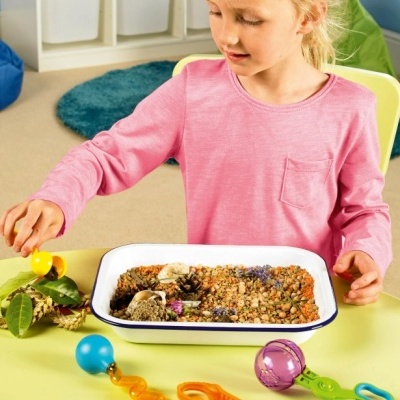 criança loira com camisola rosa brinca com brinquedos coloridos e textura de grãos numa mesa verde