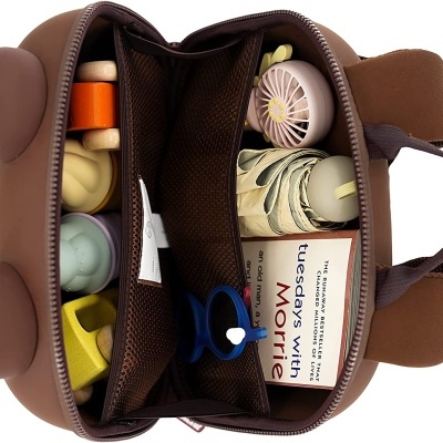 Mochila infantil castanha em forma de ursinho aberta mostrando interior com brinquedos e livro