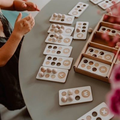 Jogo educativo de madeira com cartas numeradas e letras, bolas de madeira e mão de criança.