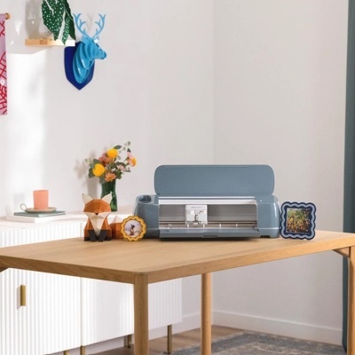 Impressora de recorte azul clara sobre mesa de madeira com decorações variadas