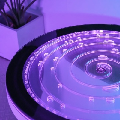 Planta em vaso branco ao lado de superfície redonda transparente com luz roxa