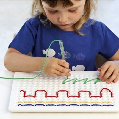 Criança a usar brinquedo educativo com base branca e cabo transparente criando padrões coloridos.