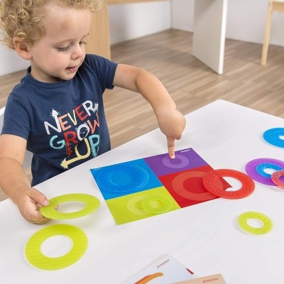 Criança brincando com anéis de plástico coloridos sobre mesa branca