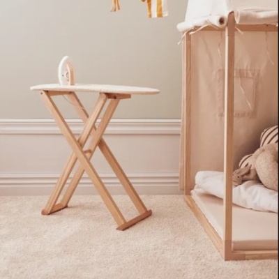 Mesa de passagem de madeira clara com ferro de engomar branco e berço de madeira ao lado