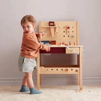 Criança com bancada de trabalho infantil em madeira clara com peças coloridas e tapete cinza