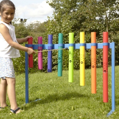 Criança a tocar xilofone de tubos coloridos em suporte azul no exterior, em relvado.