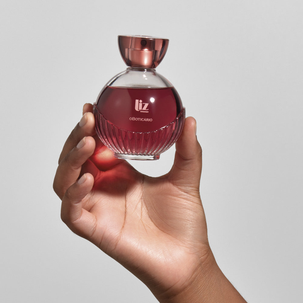 Frasco redondo de perfume rosa e vermelho segurado por uma mão