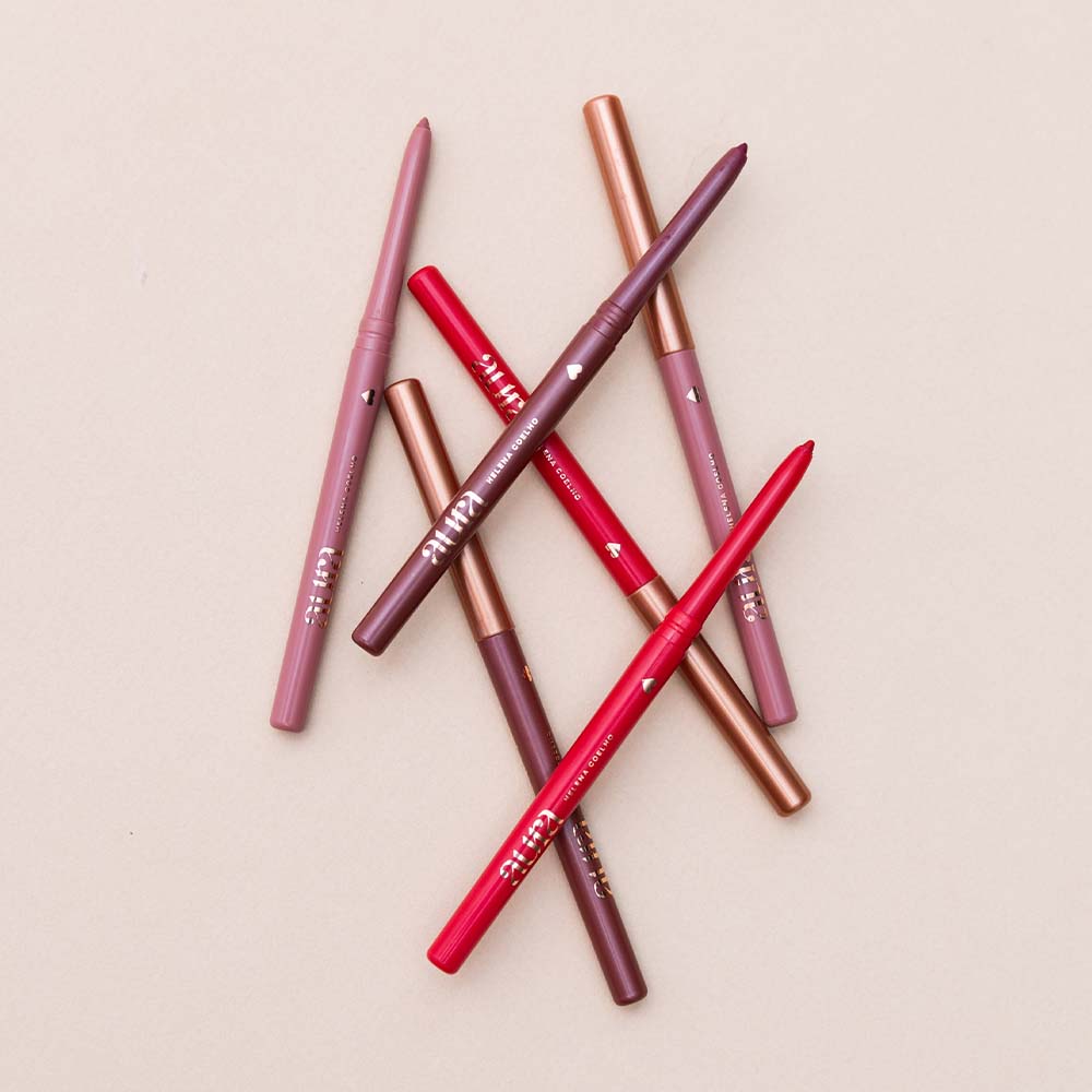 Seis lápis de lábios em tons variados sobre fundo bege.