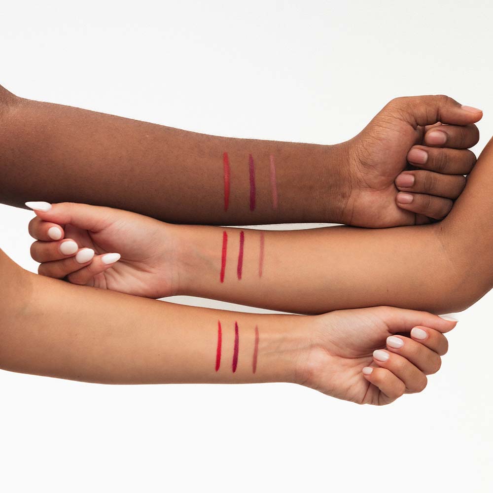 Três braços de tons de pele diferentes com traços de lápis de lábios em várias cores