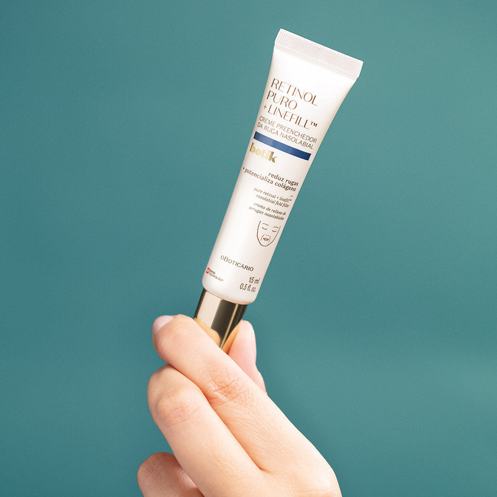 Botik Retinol Puro + LinefillTM Creme Preenchedor da Ruga Nasolabial 15ml Tubo branco de produto cosmético com tampa dourada segurado por mão sobre fundo azul esverdeado