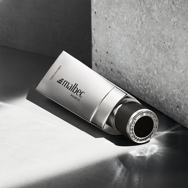Frasco de perfume Malbec Magnetic prateado com tampa preta sobre superfície cinza.