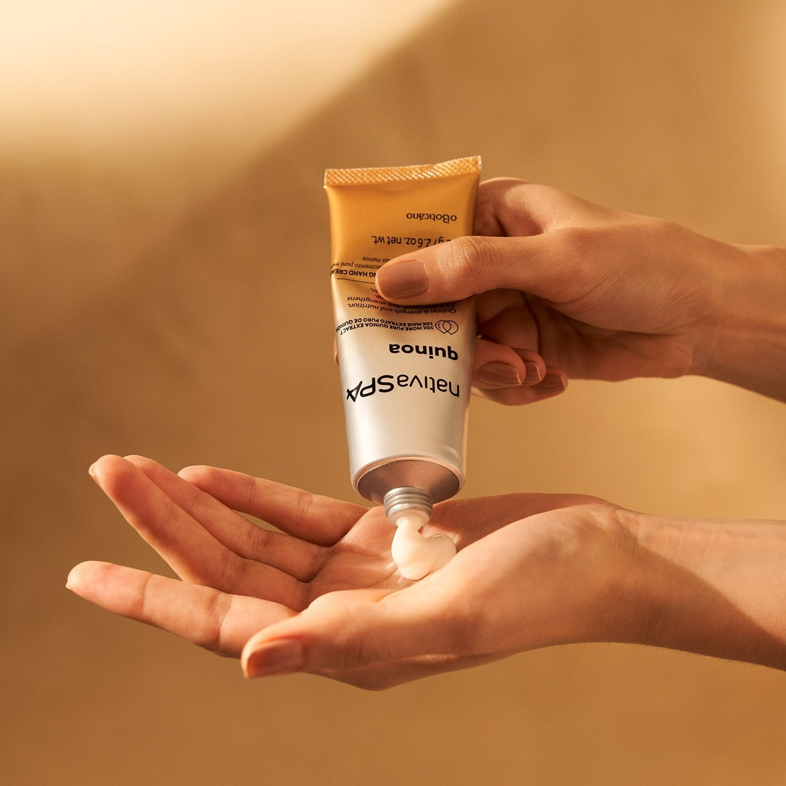 Nativa SPA Creme Mãos Antissinais Quinoa 75g Mãos femininas a aplicar creme de tubo metálico dourado NATURASPA quínoa
