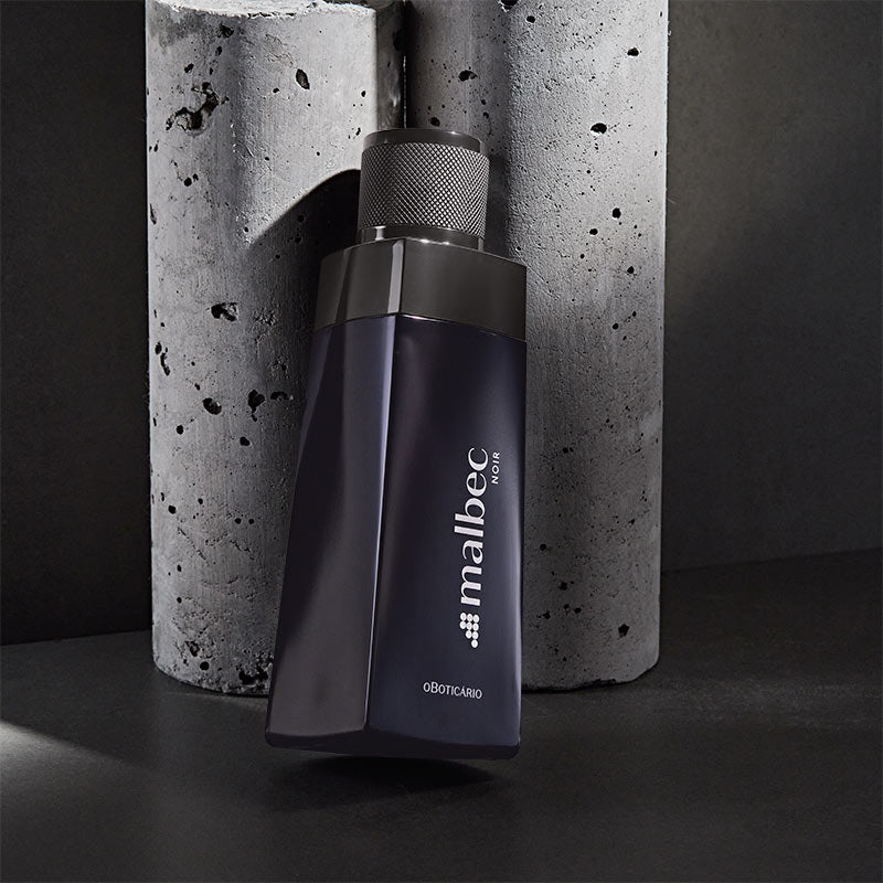 Frasco de perfume Malbec Noir preto com tampa texturizada sobre fundo cinzento de cimento