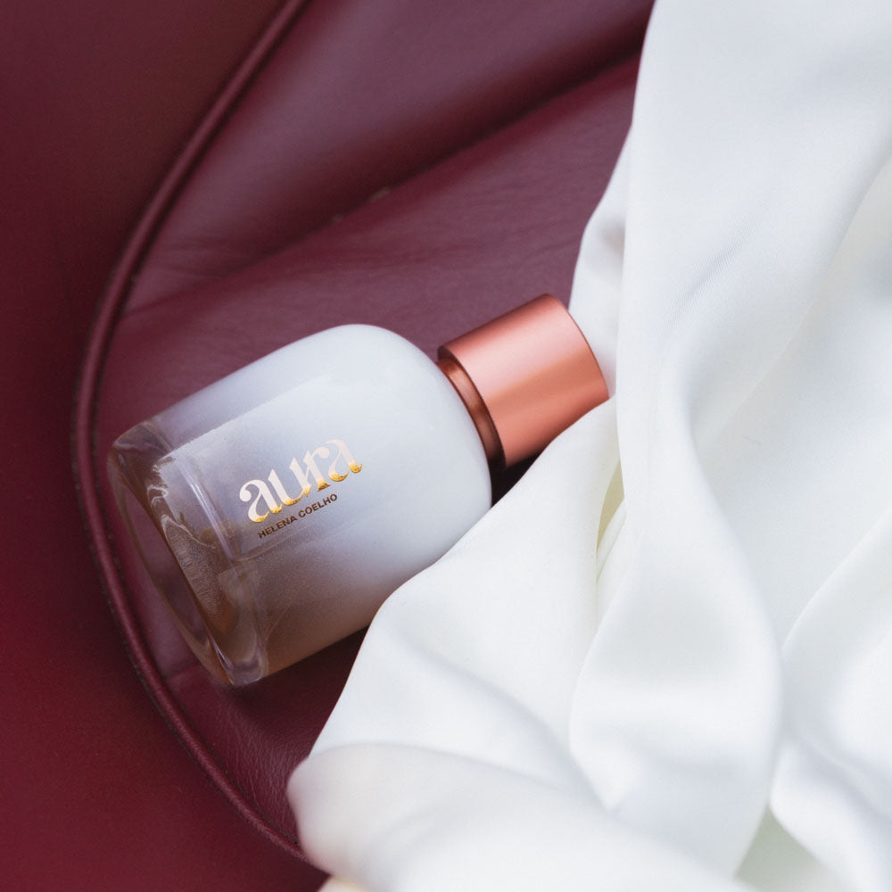 Frasco de perfume branco com tampa cobre sobre couro vermelho e tecido branco