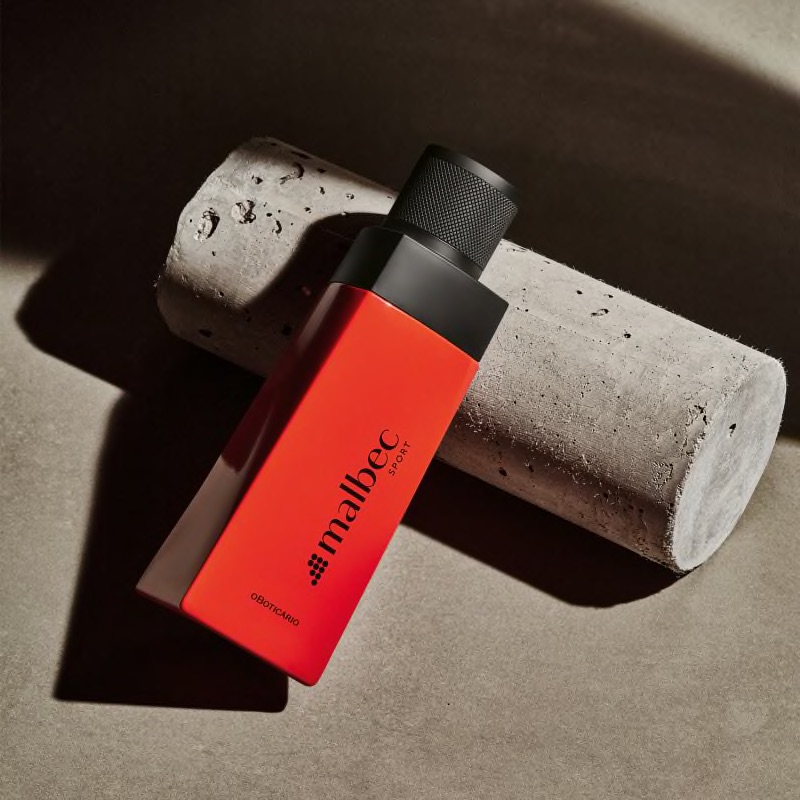 Malbec Sport Eau de Toilette 100ml Frasco vermelho de perfume Malbec O Cachorro com tampa preta sobre objeto de cimento