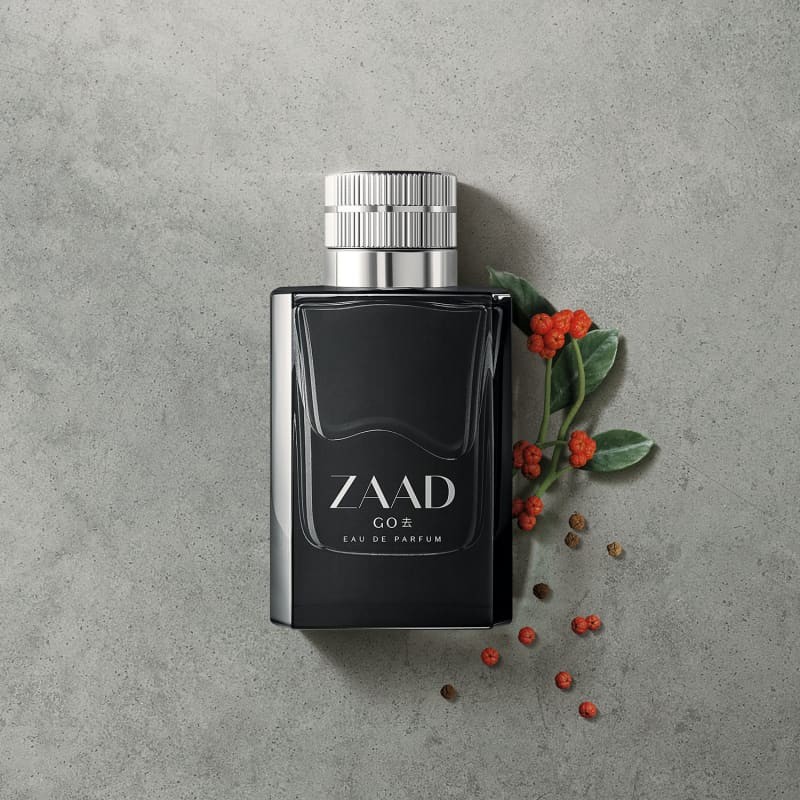 Zaad Go Eau de Parfum 95ml Frasco preto de perfume Zaad Co 28 sobre superfície cinza com ramos verdes e bagas vermelhas