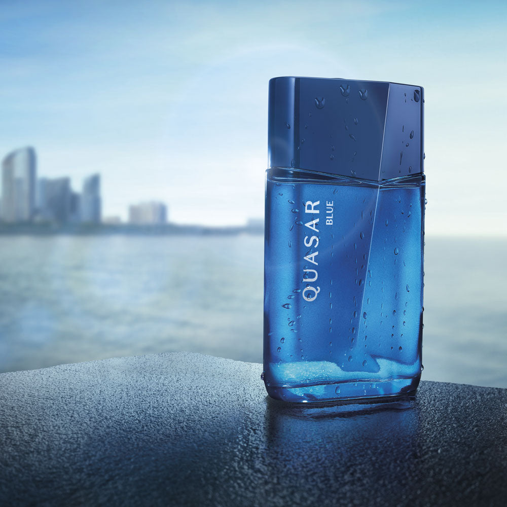 Frasco de perfume azul QUASAR BLUE em superfície molhada junto a água e edifícios desfocados