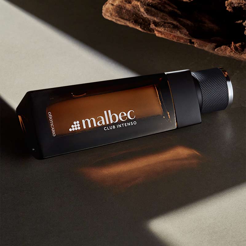 Frasco de perfume Malbec Club Intenso em vidro castanho com tampa preta sobre superfície cinzenta.