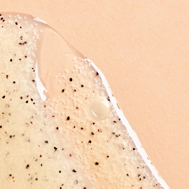 Monoï Óleo Esfoliante Corpo Bronzeado 150ml Gel translúcido com partículas negras e brancas sobre fundo rosa claro