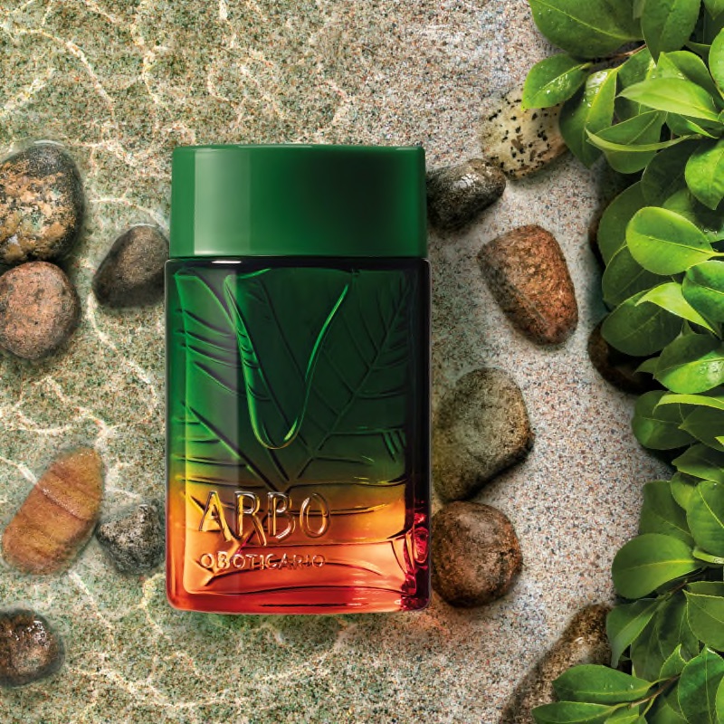 Arbo Liberté Eau de Toilette 100ml Frasco de perfume verde e laranja com tampa verde sobre pedras e folhas verdes