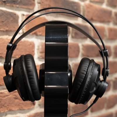 Auscultadores pretos com almofadas acolchoadas num suporte preto frente a uma parede de tijolos.