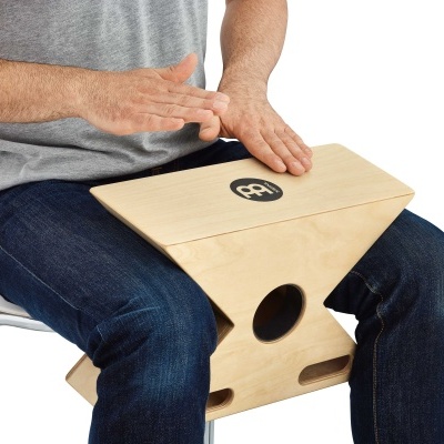 Pessoa tocando cajón de madeira clara, sentada