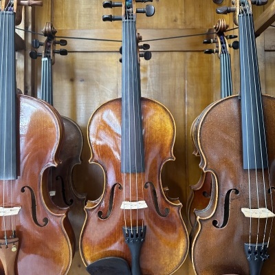 Quatro violinos pendurados em suporte de madeira com fundo de painel de madeira clara