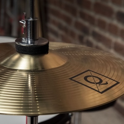 Prato de bateria dourado com símbolo preto e suporte metálico numa sala com parede de tijolos